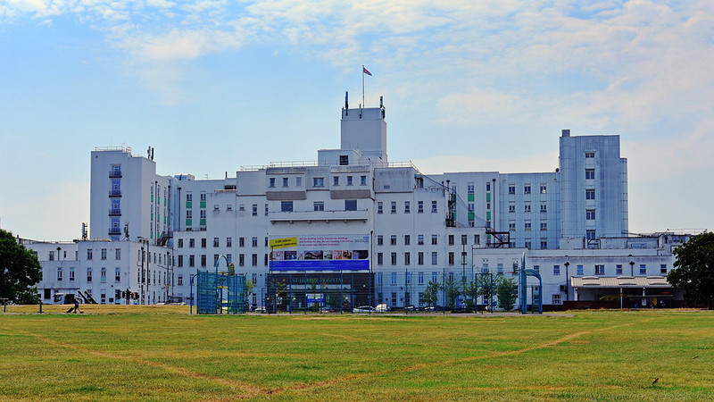 Wide view of white hospital buildings showing grass below and sky above.
