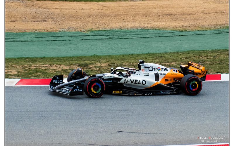 McLaren F1 car pictured from the left side taking the corner with the runoff pictured above the car, captured from the far side of the track