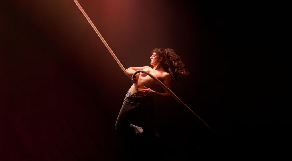 A woman in dark theatrical lighting holding on to a rope