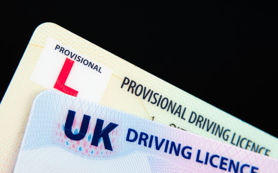 The left corners of a UK driving licence and a provisional driving licence overlaid on one another. The picture has a black background.
