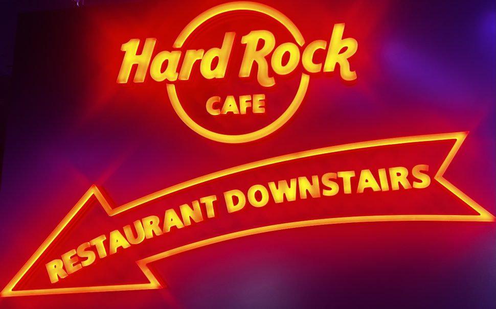 Illuminated writing in red saying Hard Rock Cafe Restaurant downstair with an arrow which is also illuminated in red. it is glowing