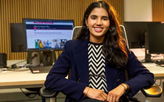 Photo of Krisha Dhanasekaran sitting on a chair and smiling at the camera