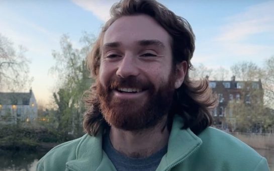 A smiling photo of the Cambridge Blue Boat captain, Seb Benzecry. He is in the foreground, with trees and houses in the background.