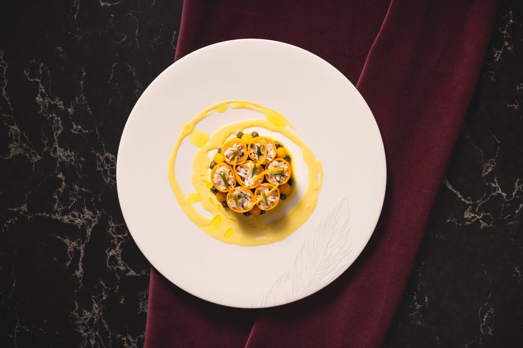 Dramatic shot of dish presented for Sally Abé's celebration of International Women's Day at The Pem. There is the main dish which includes 7 spheres containing ingredients. There is a yellow sauce dressed on the plate.