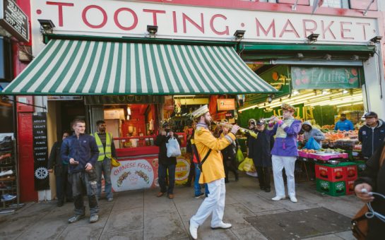 People in outfits playing instruments outside Tooting Market in London