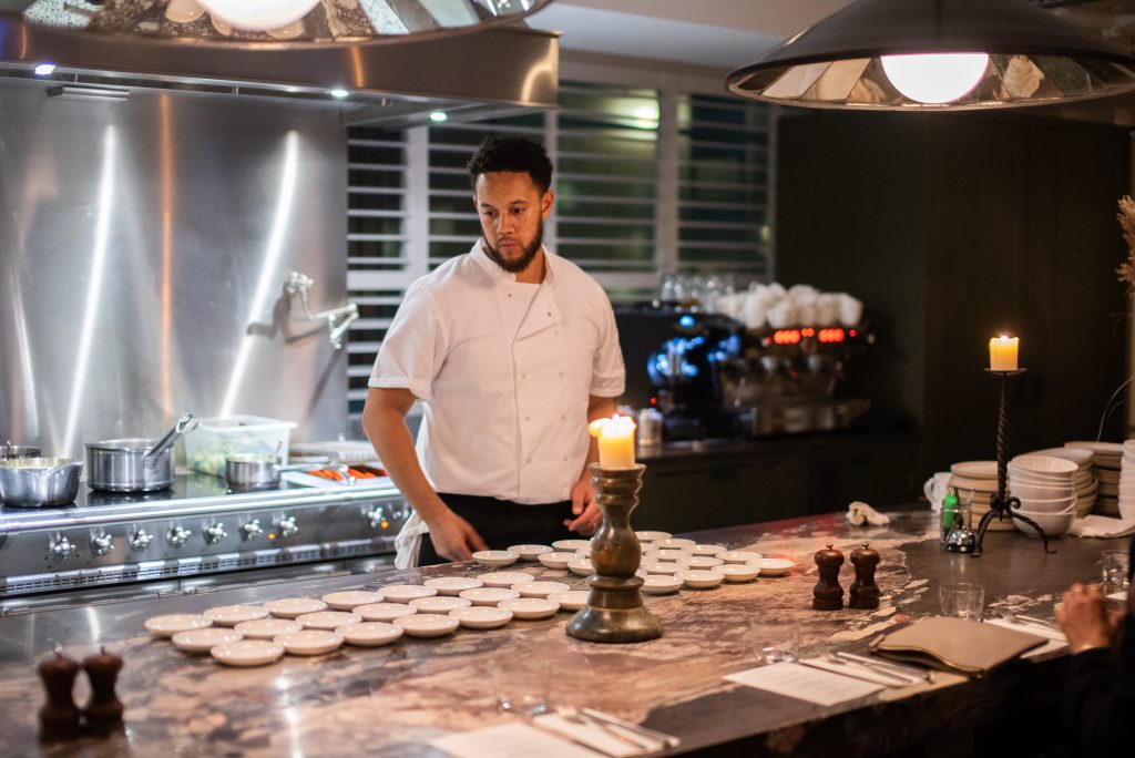 A chef stands looking at a number of empty dishes on the pass.