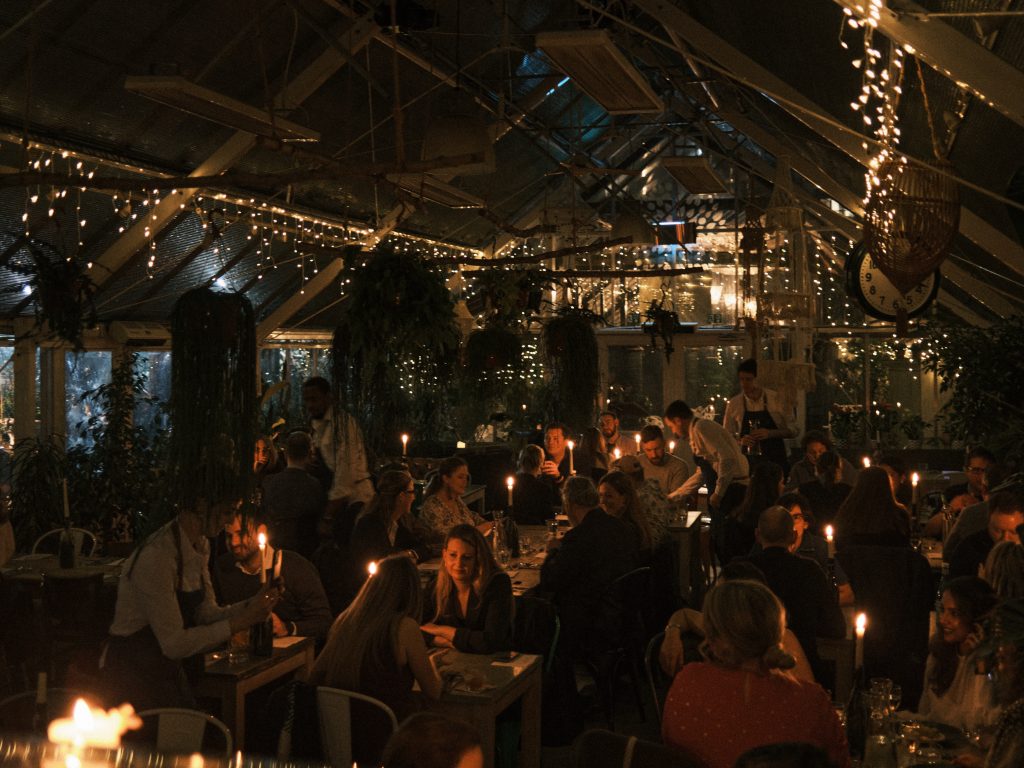 A full restaurant with each table lit by a candle. The picture of dark as the only other source of light comes from fairy lights.