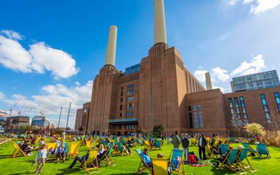 Image of Battersea Power Station in Summer with many people sat outside on deck chairs.