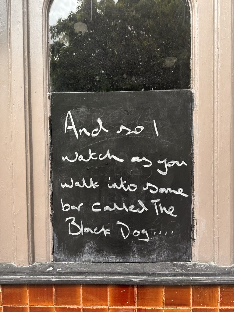 Taylor Swift lyrics from "The Black Dog" written on black chalk board in window 
