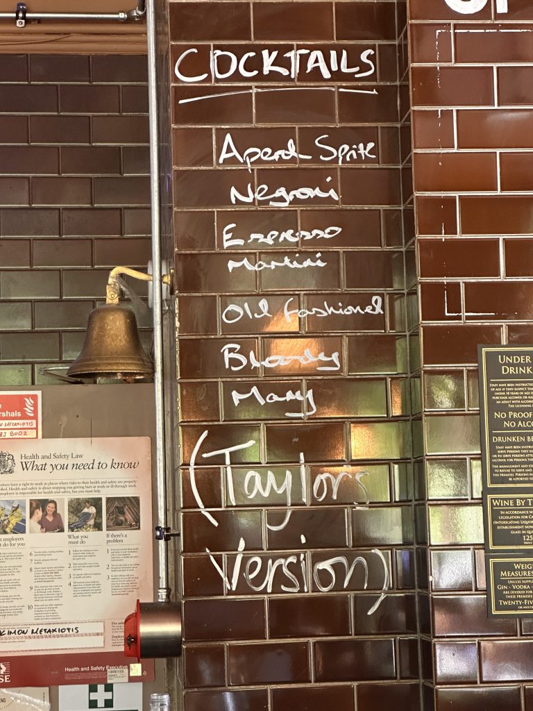 Drinks menu written on brick wall with Taylor's Version written at the end 