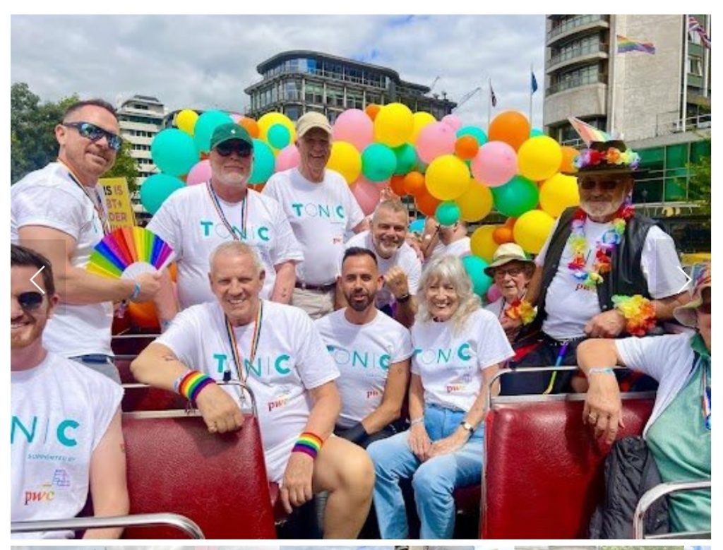 A group of older LGBTQIA+ people and Tonic residents, surrounded by multicoloured balloons and wearing t-shirts that say "Tonic" 