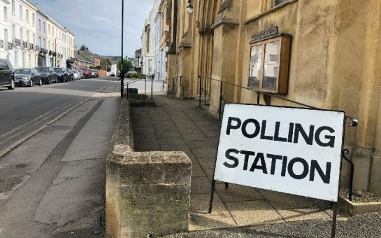 A sign reading "Polling Station" is set outside a ramped entrance to a building on a quiet street.