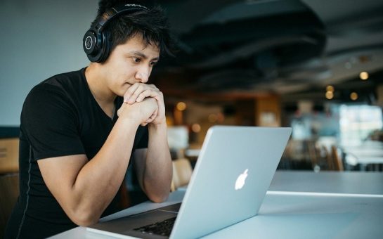 A young man looking at his laptop, wearing his headphones