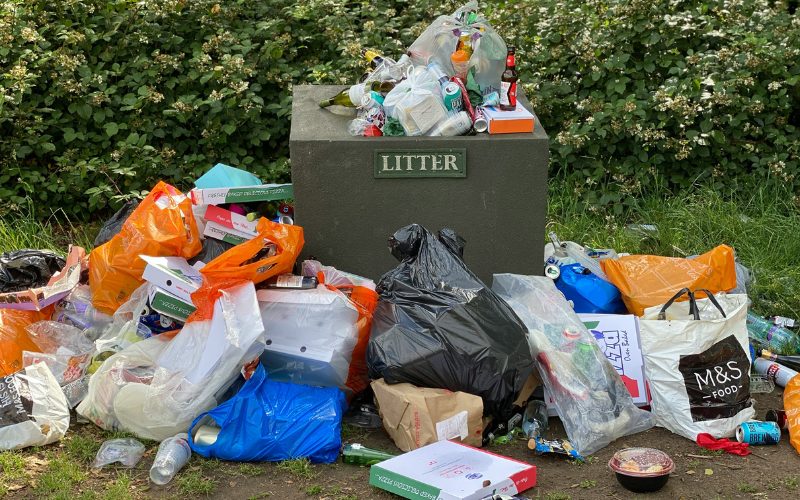 Picture showing example of London fly-tipping of over-flowing bin with several rubbish bags put next to it