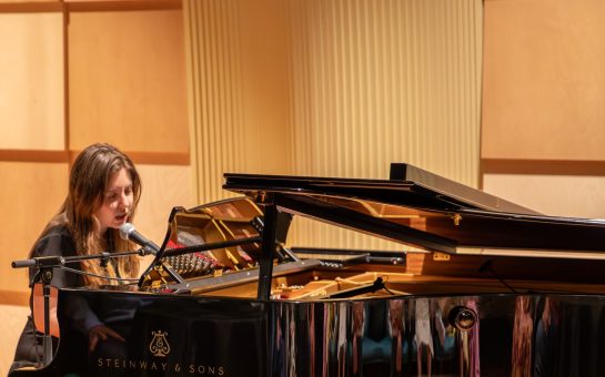 A woman, Ruxy, playing a piano and singing.