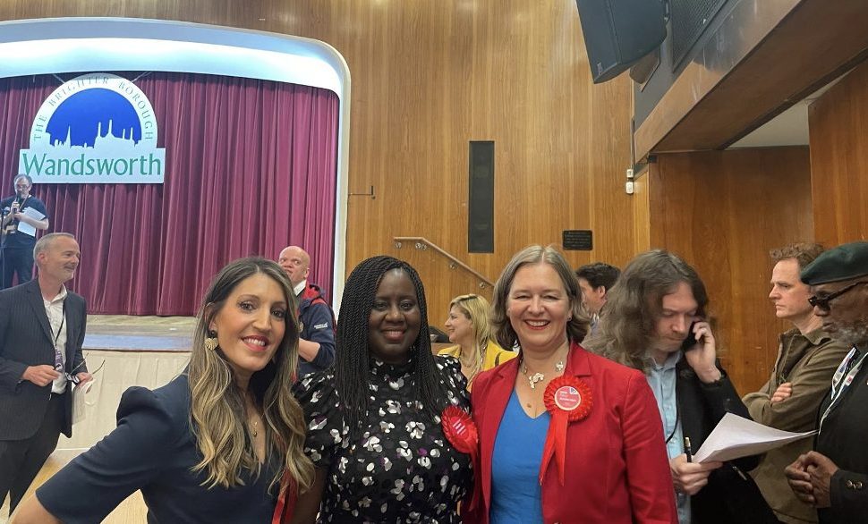 Three women wearing red rosettes smiling at camera