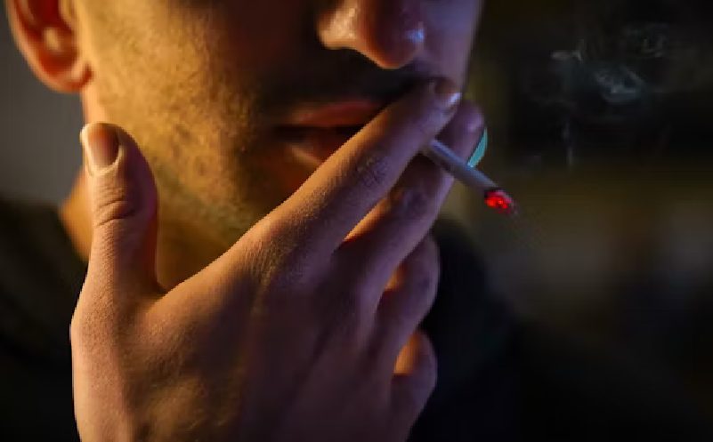 person holds lit cigarette to their mouth