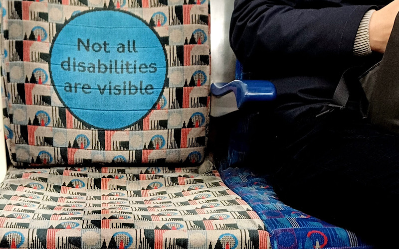 A grey seat on the London Underground that says "Not all disabilities are visible"