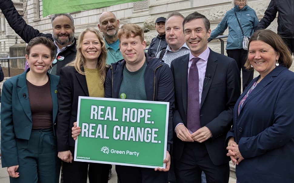 Herne Hill by-election candidate Paul Valentine with Green Party leaders Carla Denyer and Adrian Ramsay, as well as the two other Green MPs and other supporters. They are holding a placard saying "Real Hope. Real Change".