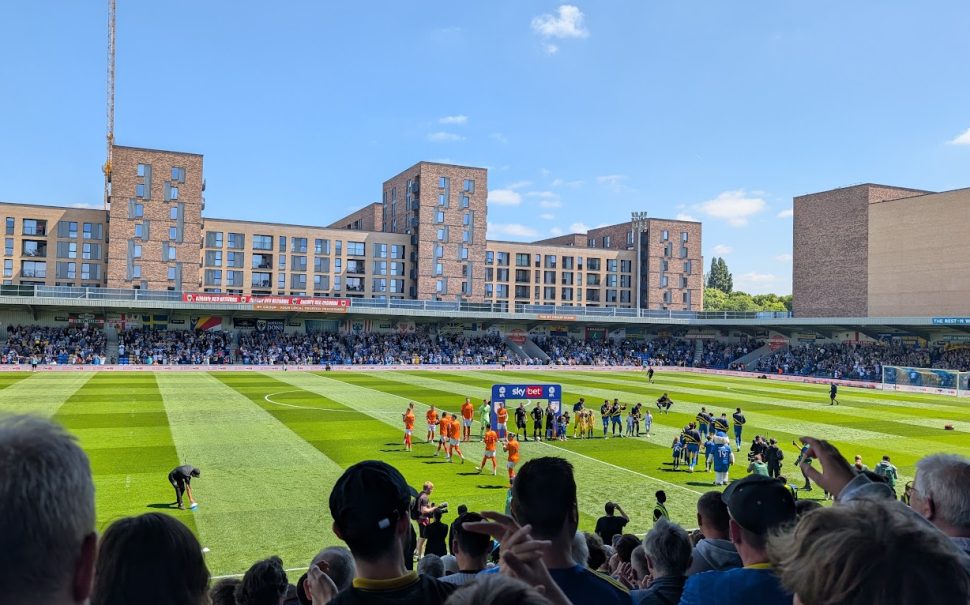 An image of AFC Wimbledon's Plough Lane stadium interior as the teams walk out onto the pitch.
