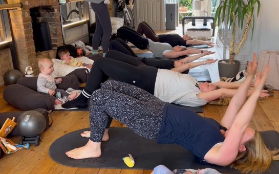A group of five mums take part in a pilates class, with their babies watching on.