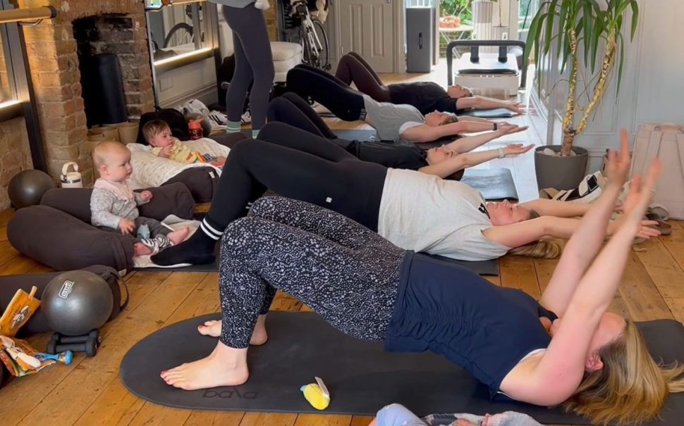A group of five mums take part in a pilates class, with their babies watching on.