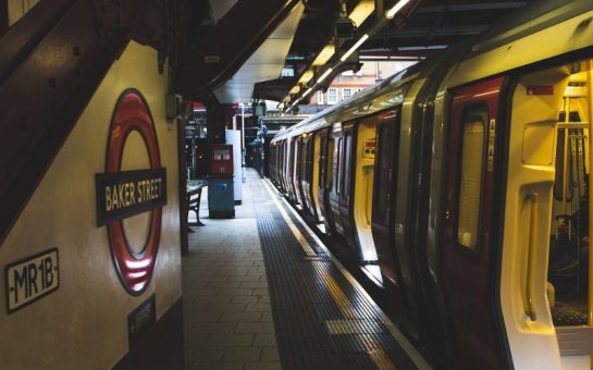 A darkly-lit undeground station with a train with open doors.
