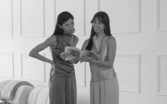 Two sisters holding a magazine whilst smiling.