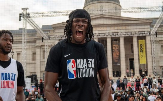Two basketballers mid-game with the one on the right side exclaiming in joy with Trafalgar Square in the backdrop of the photo.