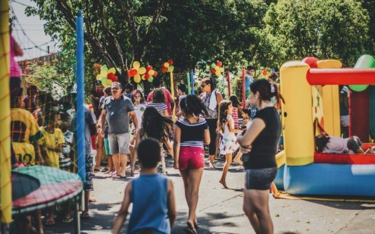Photo of crowds at a fair outside. There is a bouncy castle.