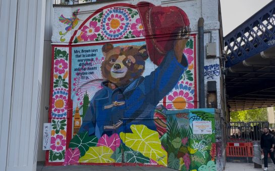 Paddington Bear Mural holding his red hat in the air by Waterloo Station