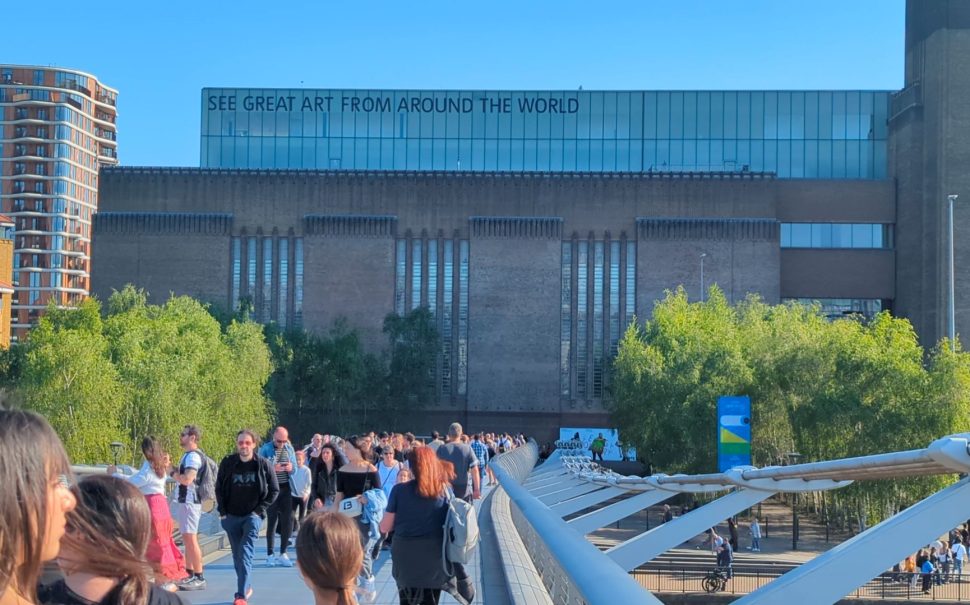 Crowds of people crossing a bridge walking towards the Tate Modern