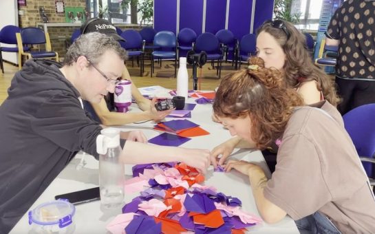 A man and two women creating origami flowers together at a table.