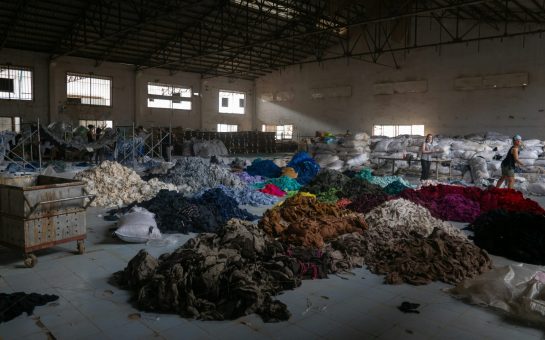 Image of piles of used clothes on a warehouse floor.