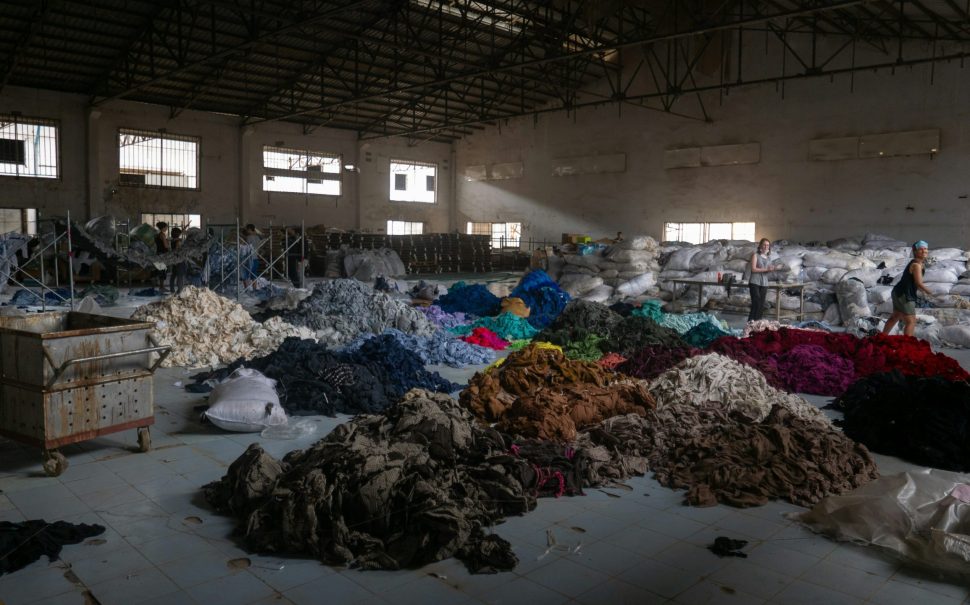 Image of piles of used clothes on a warehouse floor.