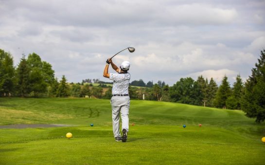 Golfer wearing a white outfit hitting a shot with a driver looking out onto the green golf course