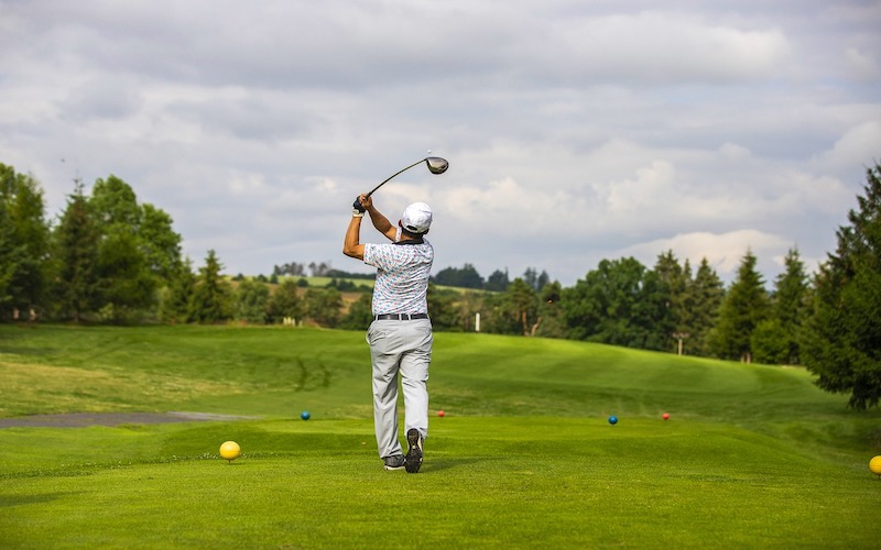 Golfer wearing a white outfit hitting a shot with a driver looking out onto the green golf course