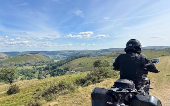Man on motorbike facing out on the countryside in black motorbike gear and on black motorbike