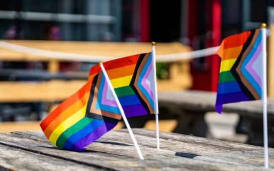A picture of three small Pride flags on a bench.