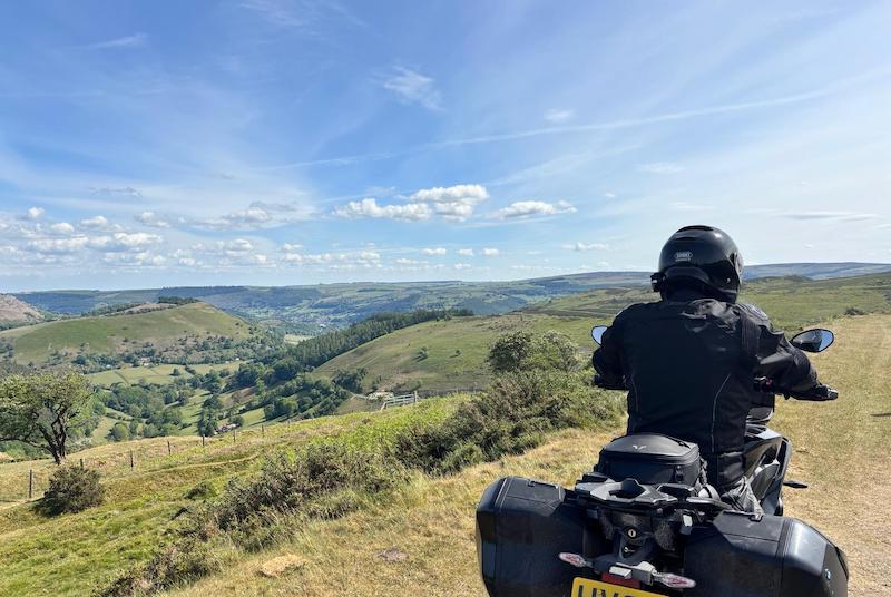 Man on motorbike facing out on the countryside in black motorbike gear and on black motorbike
