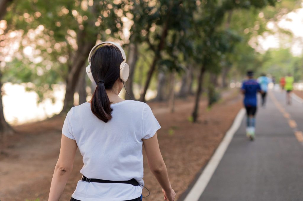 Image of a woman wearing headphones walking on a pathway in a park