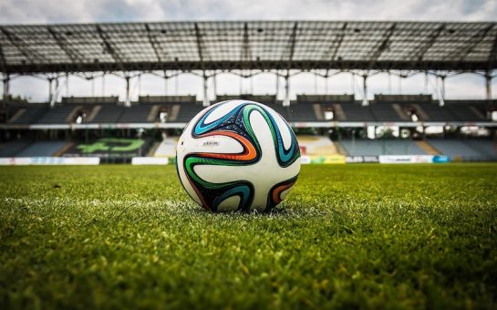 Football on the pitch with stadium seating in the background. (Picture credit: Jarmoluk)