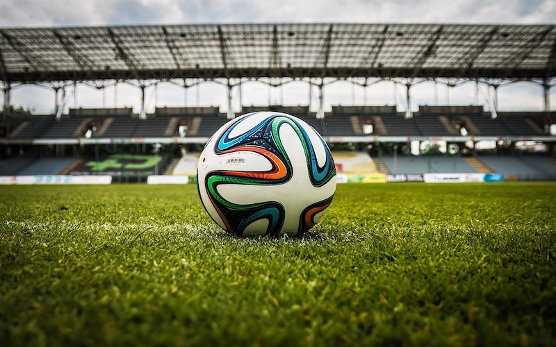 Football on the pitch with stadium seating in the background. (Picture credit: Jarmoluk)