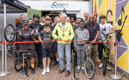 The front of Carney's Cycles with staff and young people with bikes behind a red ribbon, which is being cut.