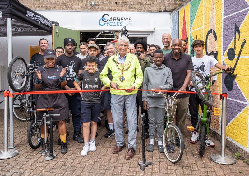The front of Carney's Cycles with staff and young people with bikes behind a red ribbon, which is being cut.