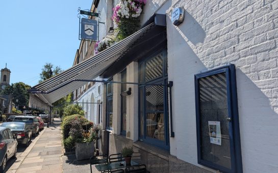 The Carpenter's Arms exterior, with a blue traditional pub sign and blue and white striped canopy sitting above outside furniture.