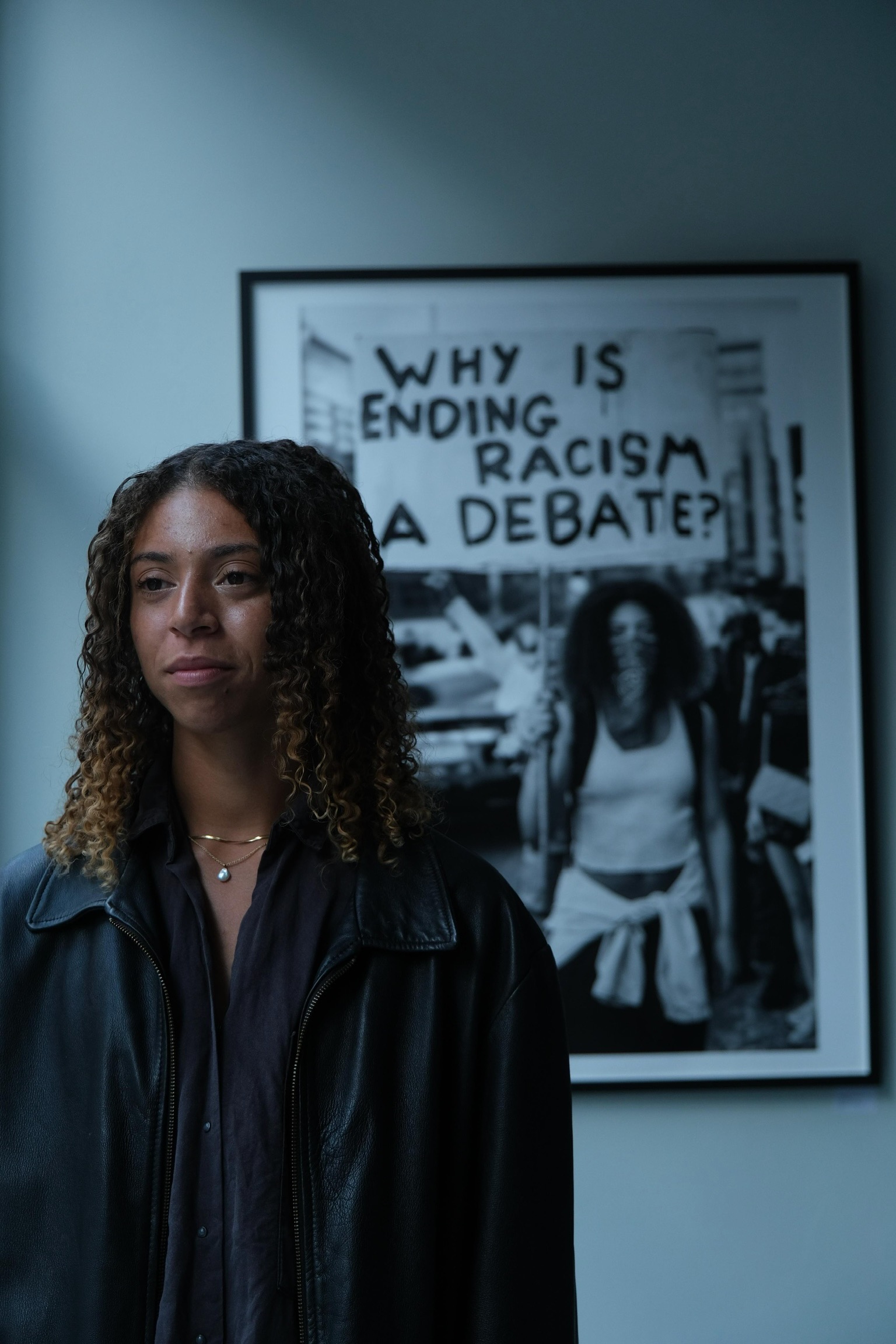 A photo of Darcy Bourne stood in front of a picture in an art gallery. She has a reflective look on her face.