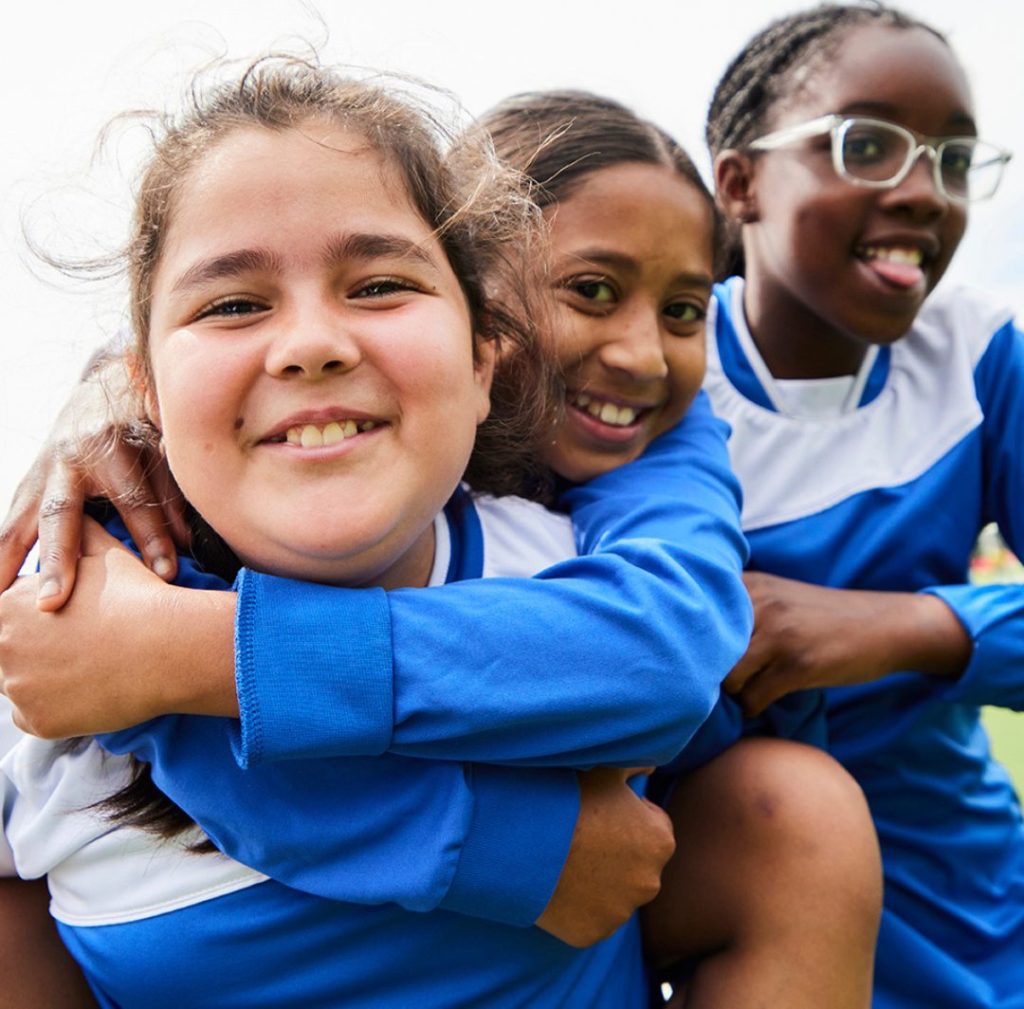 Three young female football players smile at the camera.