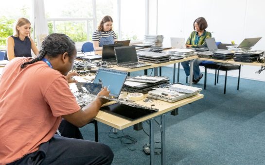 4 people sitting around a table, fixing and working on laptops