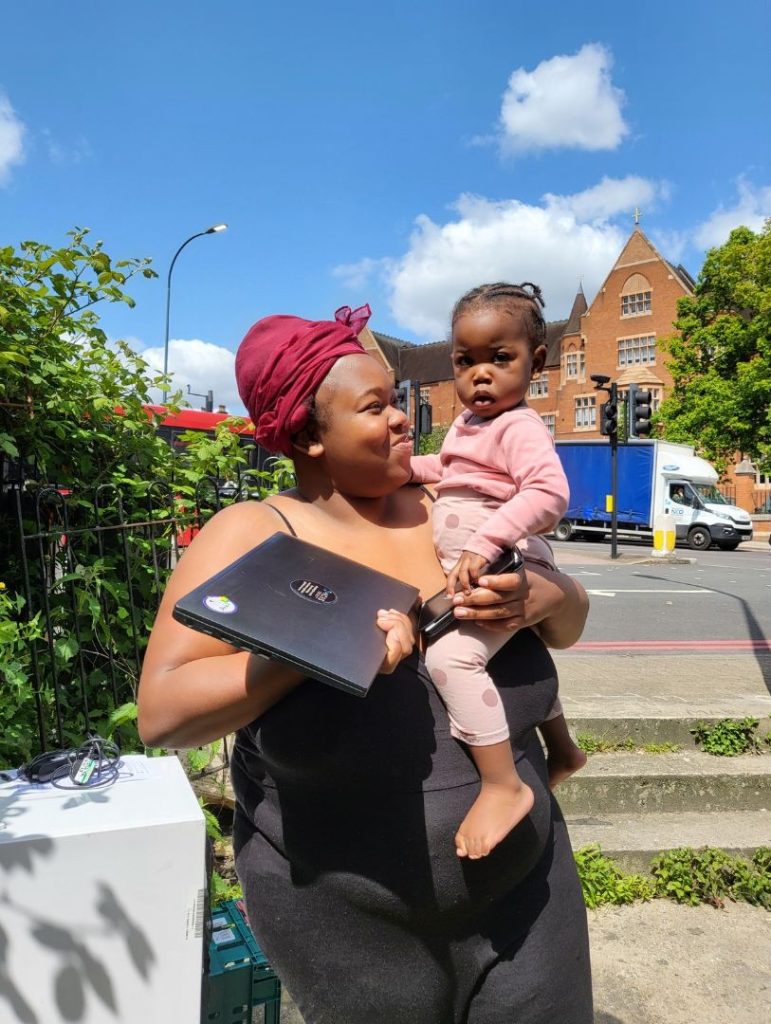 A beneficiary of Community TechAid with her new laptop in hand and a baby in her arms, picture by Community TechAid
